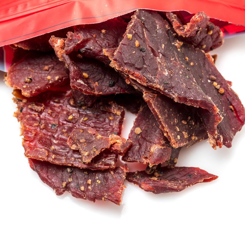 Beef Jerky close up coming out of it bag on white from above