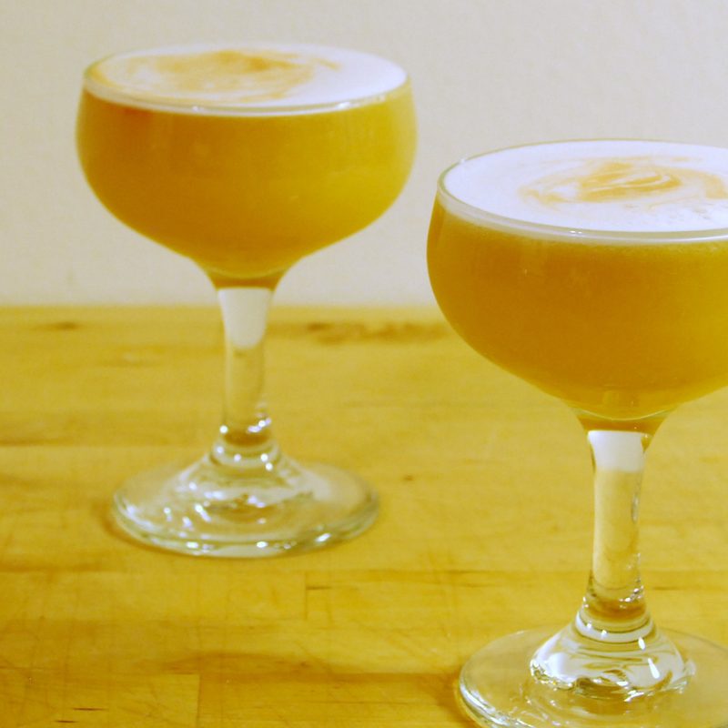 Two glasses of kumquat whiskey sour on a wooden table