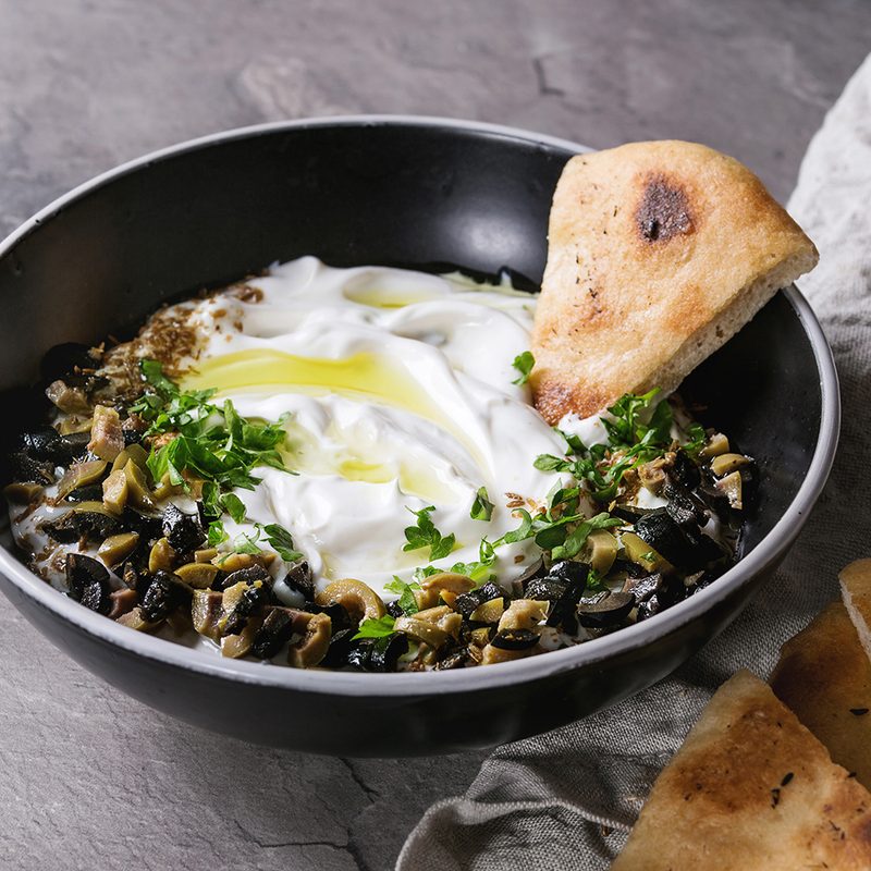 Mezze - Middle Eastern Lebanese cream cheese dip with olive oil, salt, herbs, olives tapenade served in black bowl with traditional pita bread