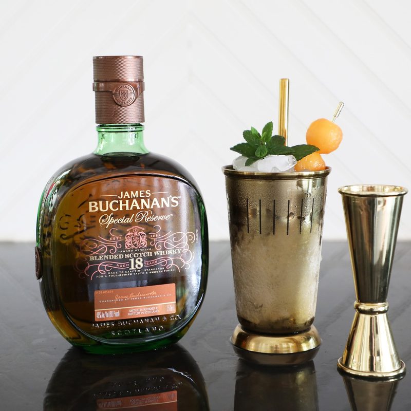 A bottle of Buchanan’s Special Reserve beside a Spring Fling Julep Cocktail with mint leaves and melon balls and a pouring sprout.