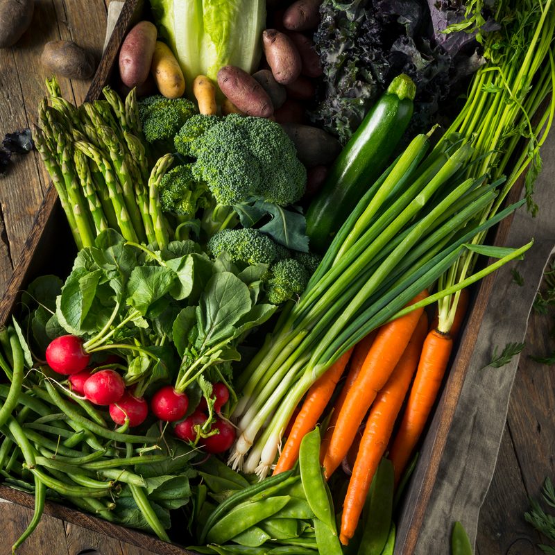 Carrots, broccoli, and spring onions among other spring vegetables laid out in a wooden table
