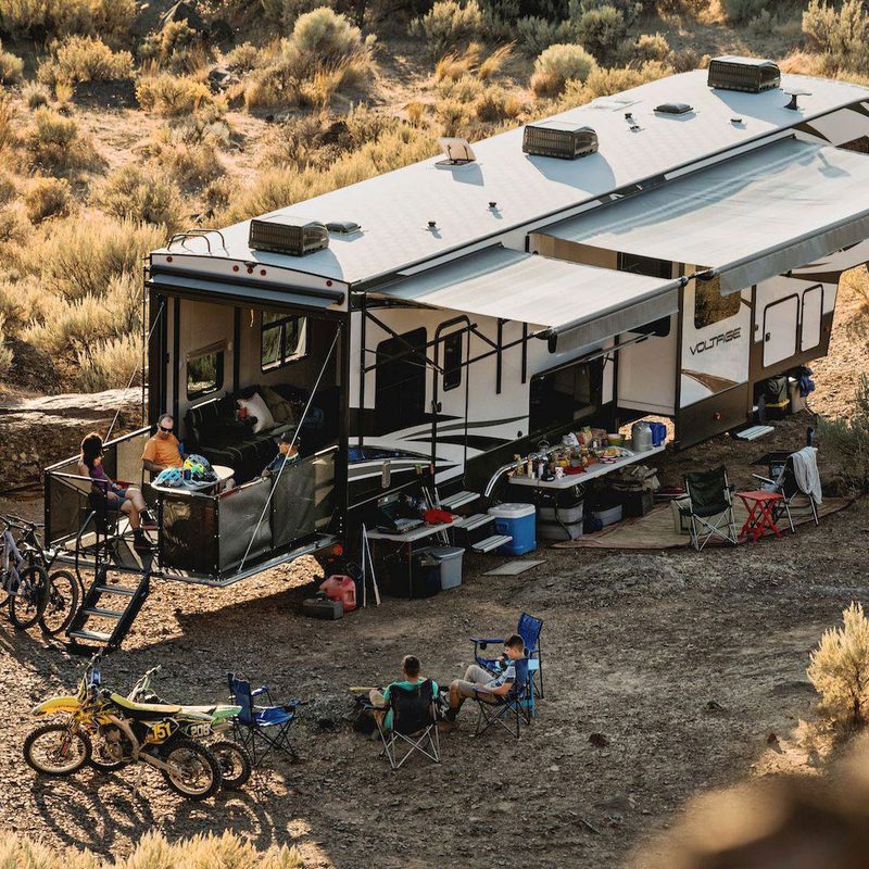 Full-sized Dutchmen RV Toy Hauler setup at a desert campsite with campers in the foreground.