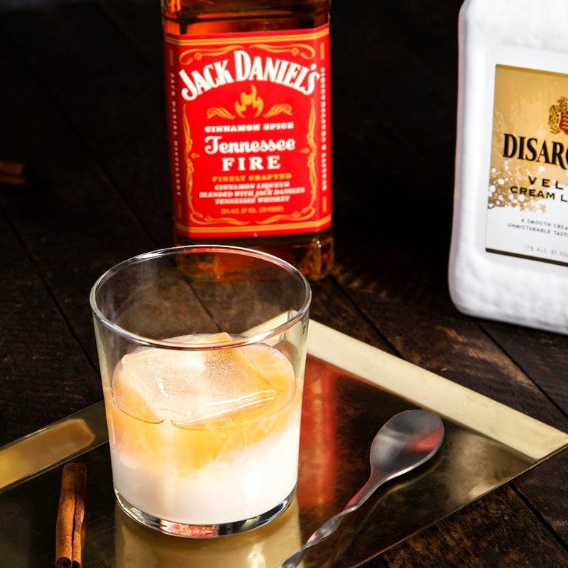 A glass of Velvet Fire Cocktail beside a spoon with Disaronno Velvet and Jack Daniel's Tennessee Fire behind it.