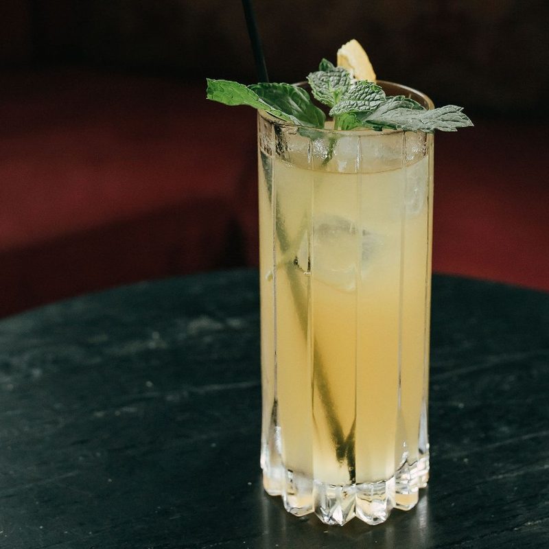A glass of Veracruz Smash Cocktail with mint sprig and straw on a table.