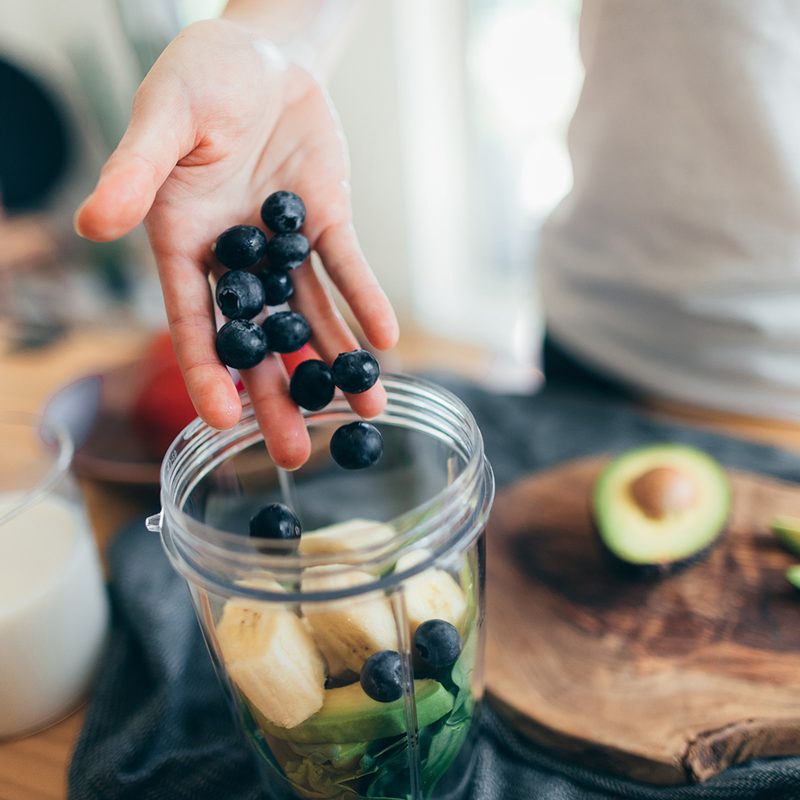Closeup shot of a female hand putting raw ingredients into a blender to make fresh fruits smoothie