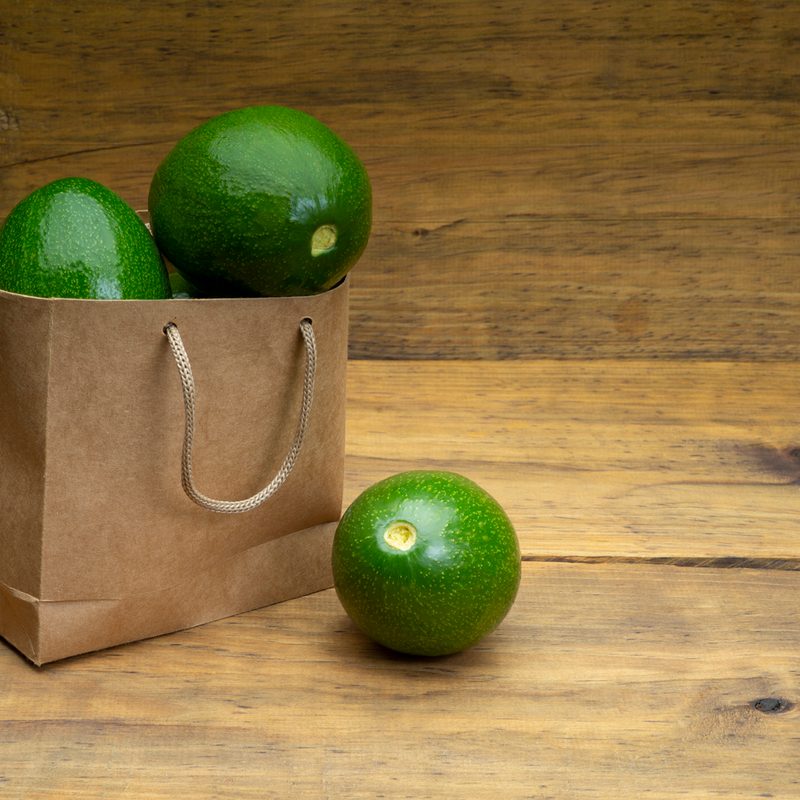 Brown bag overflowing with green avocados