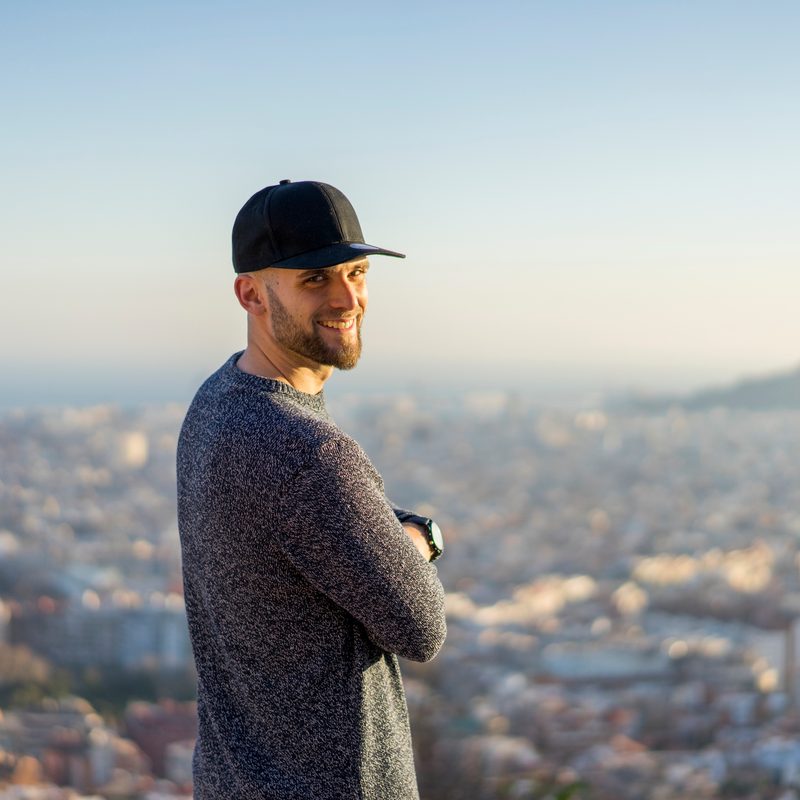 Spain, Barcelona, smiling young man standing on a hill overlooking the city