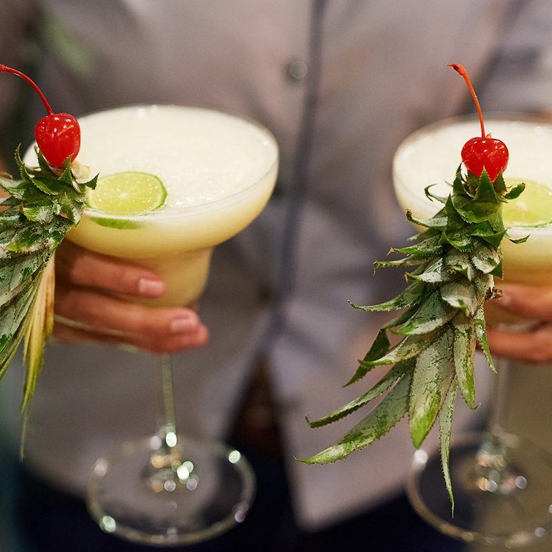 man holding two glasses of pina coladas. 
