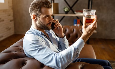 Man on his phone and inspected his glass of whiskey