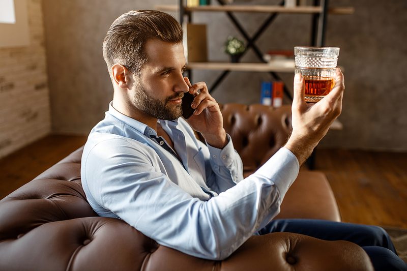 Man on his phone and inspected his glass of whiskey
