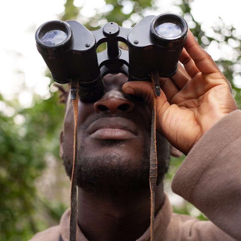 Closeup of man holding binoculars up, looking into the distance
