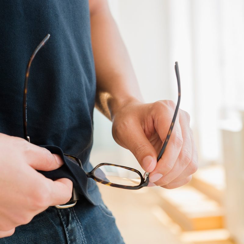man wiping glasses with t-shirt.