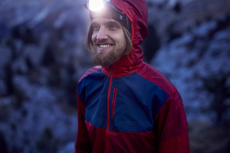 Young smiling man wearing a bright headlamp in the outdoors.