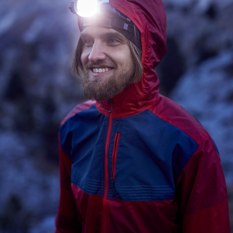 Young smiling man wearing a bright headlamp in the outdoors.