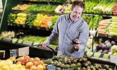 Man shopping in the produce aisle of a supermarket looking at avocados