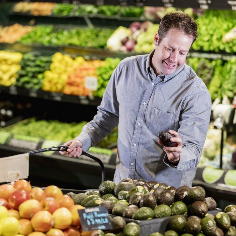 Man shopping in the produce aisle of a supermarket looking at avocados
