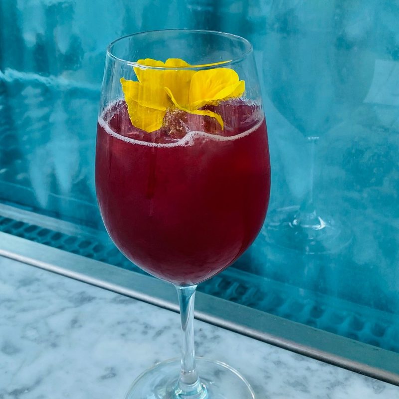 An Iaponiko Anthos cocktail with flower on a marble surface against a blue background