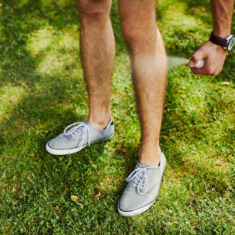 Man standing on grass, spraying insect repellent on his legs.