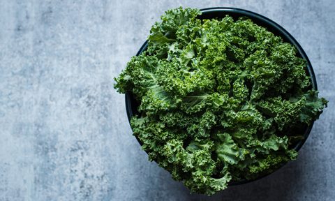 A bowl of kale on blue table.