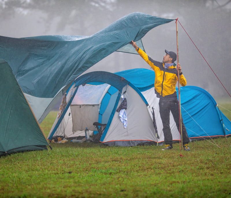 Man adjusting a tarp camping in the rain