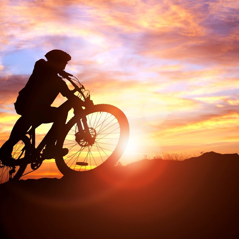 Mountain biker silhouette against the sunset concept for achievement, conquering adversity and exercising