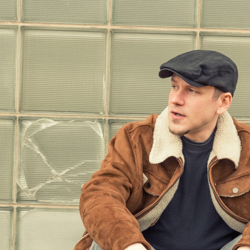 Cool guy in aviator jacket and newsie cap relaxes against a glass wall