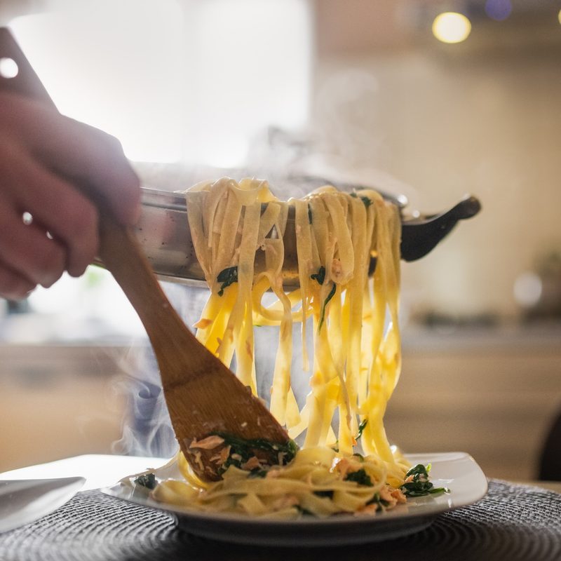 Pasta being served from a pan to plate.