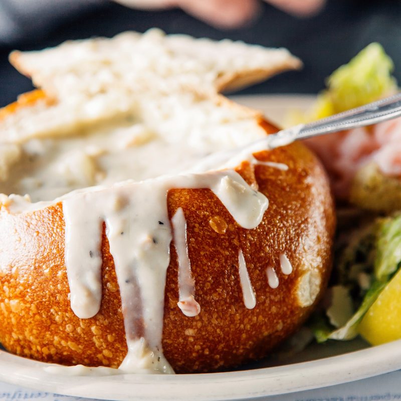 bread bowl on a plate with a utensil sticking out of it.