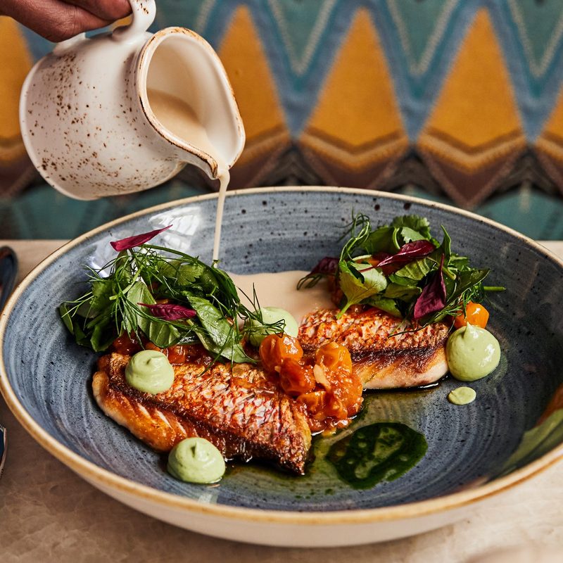 Sauce poured over grilled fish at Red Rooster Overtown