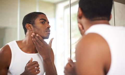 A man putting on face cream while looking in the mirror.