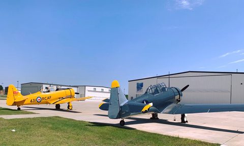 Two fighter planes, one yellow one black, sit facing an aircraft hangar.
