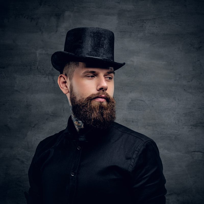 Bearded male with tattoo on his neck and top hat cylinder on head.