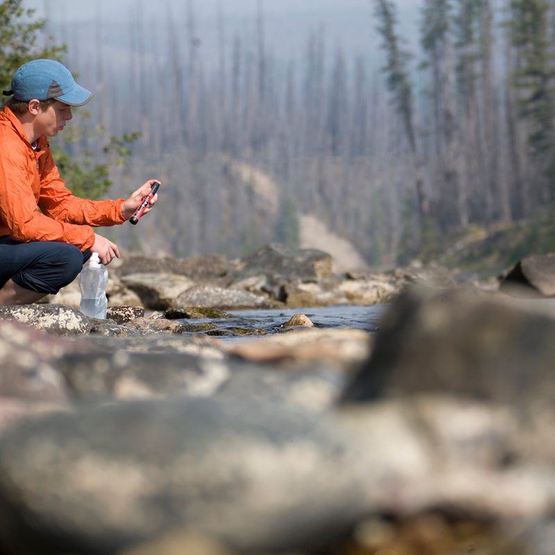 Young man using a portable water filter near a backcountry stream.