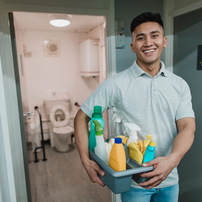 A man smiling at the camera, carrying toiletries.