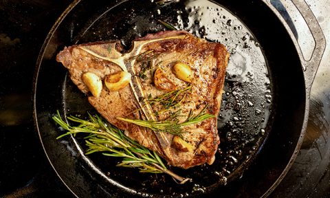 Large fatty T-bone steak in a skillet with herbs