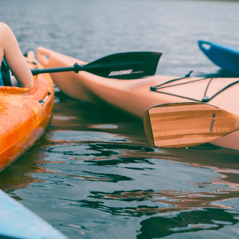 Person riding on orange kayak during daytime with other kayakers