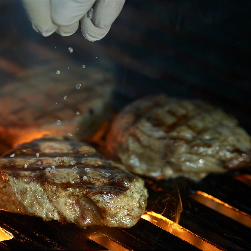 Adding salt to center of grilled steak with flames and smoke dark background