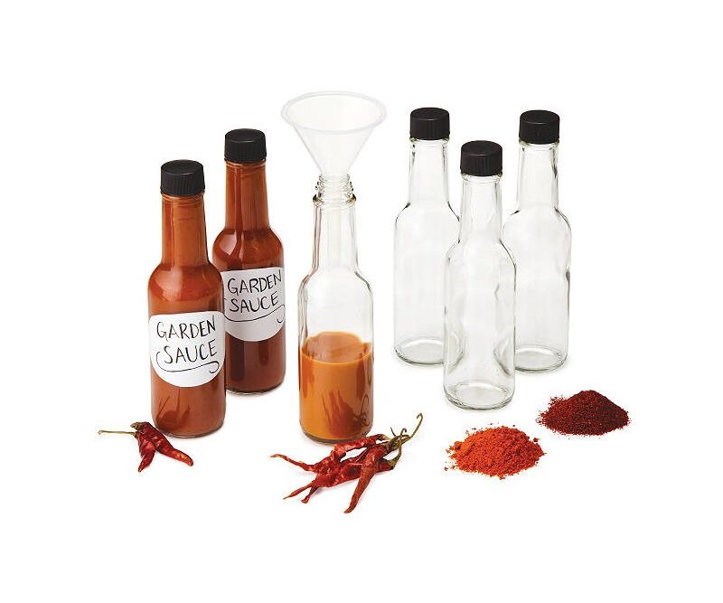 A half-full bottle with funnel in between two bottles of sauces and three empty bottles with chili and spices.