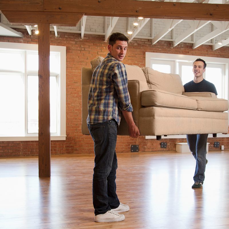 Two men carrying a sofa in an empty room.