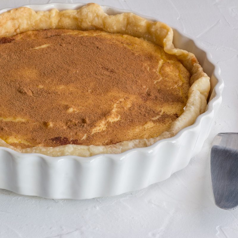 Milk tart sprinkled with cinnamon spice close up on rustic white textured background - Sweet pie crust filled with creamy custard