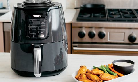 Ninja Af1oo air fryer on a kitchen counter with plate of fried chicken wings next to it.