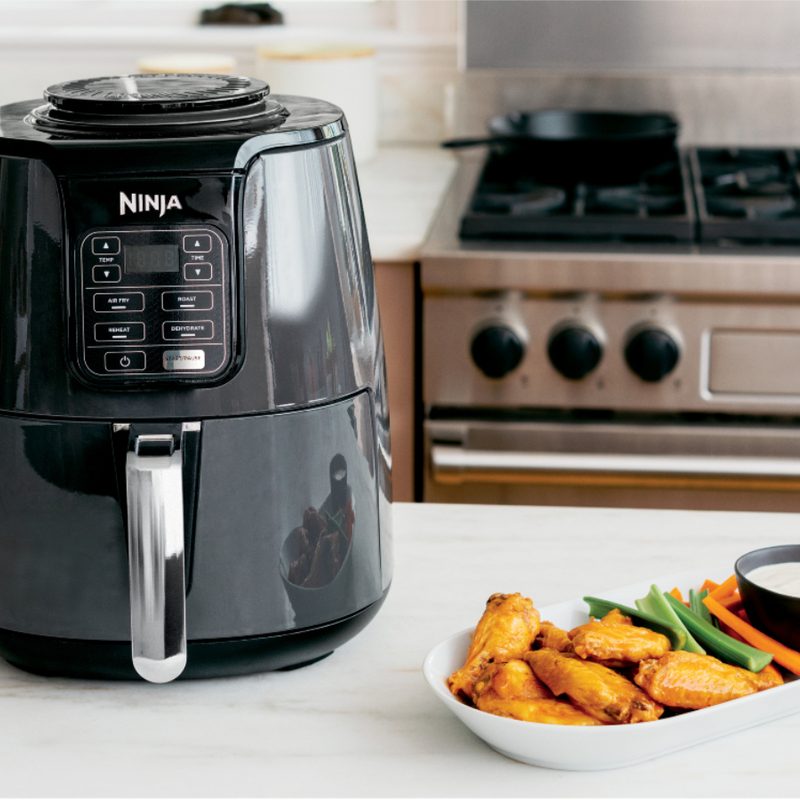 Ninja Af1oo air fryer on a kitchen counter with plate of fried chicken wings next to it.