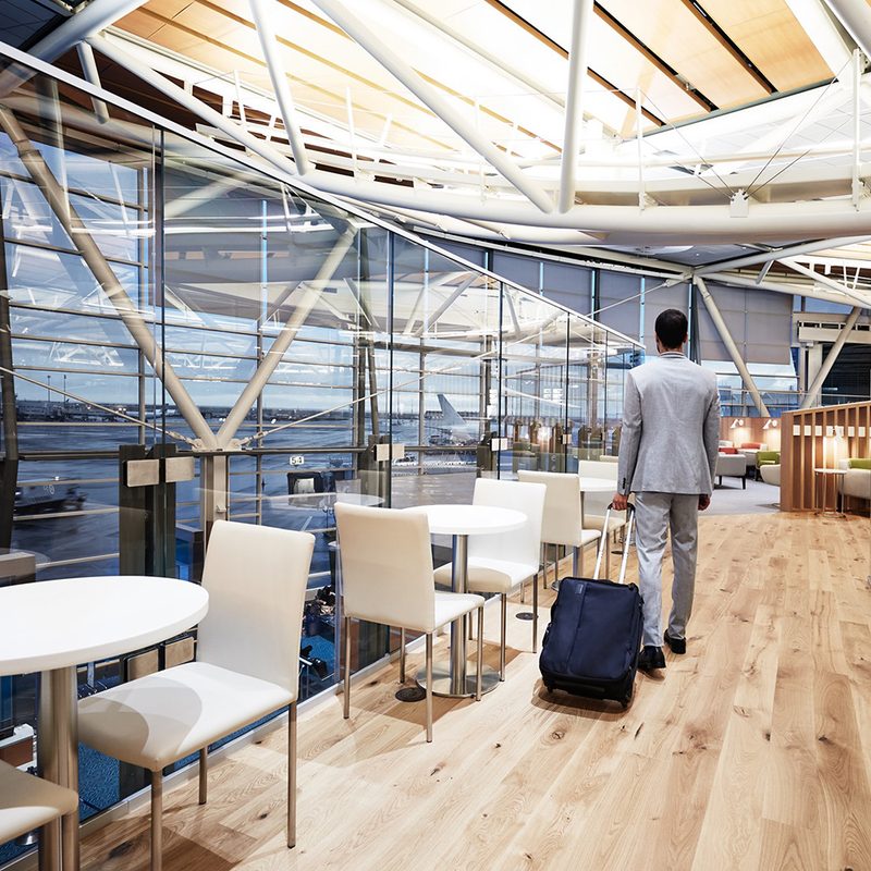 Man wheeling a rollaboard suitcase through a Priority Pass lounge in the Vancouver Airport.