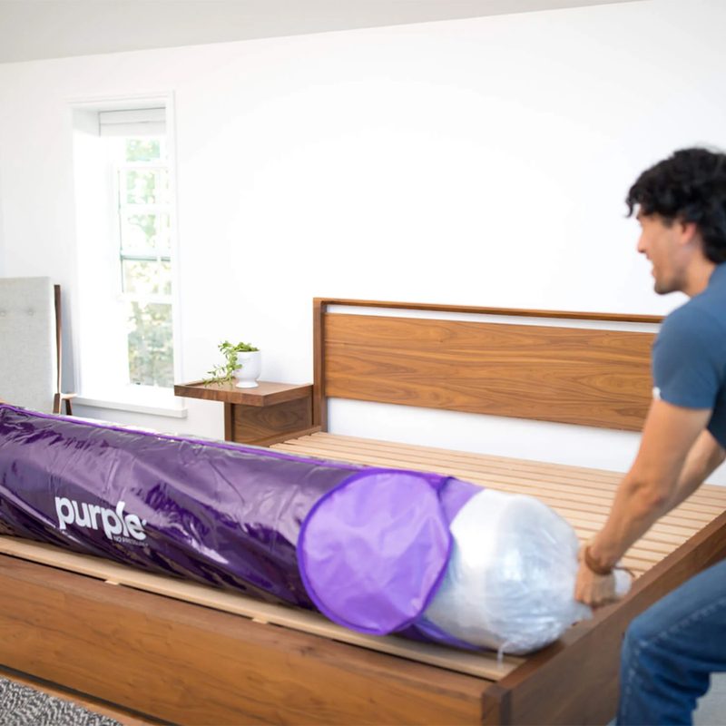 A couple setting up their Purple mattress on a wooden bed frame.