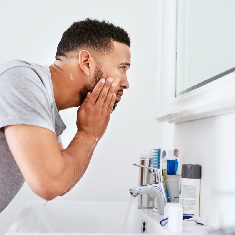 A cropped shot of a handsome young man looking worried while washing his face in his bathroom basin at home.