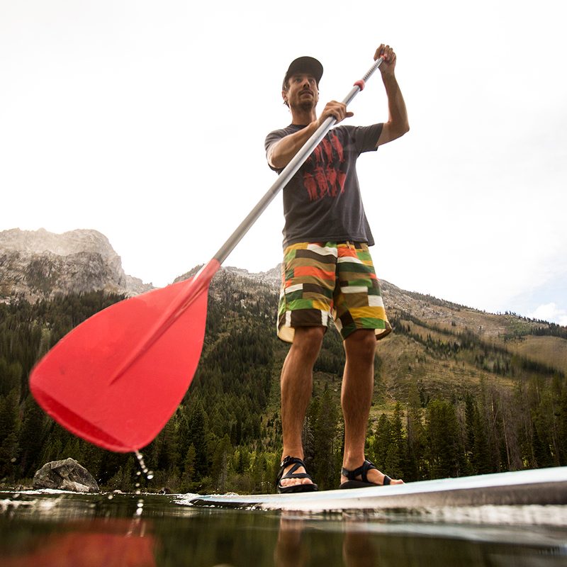 Looking up from the water at a paddleboarder, with mountains behind.