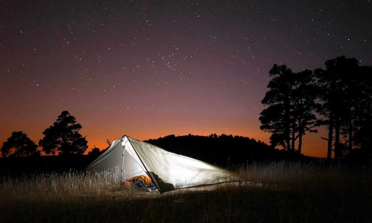 A lit up tent in an open field against a starlit sky.