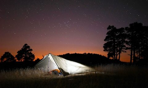 A lit up tent in an open field against a starlit sky.