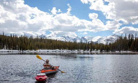 Kayaker paddling an inflatable kayak with a floating cooler in tow and snowy mountains in the background.