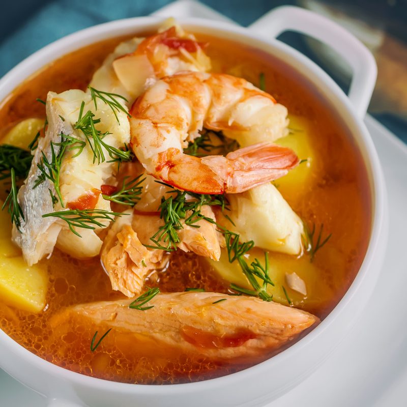 French fish soup Bouillabaisse with seafood, salmon fillet, shrimp, rich flavor, delicious dinner in a white beautiful plate.